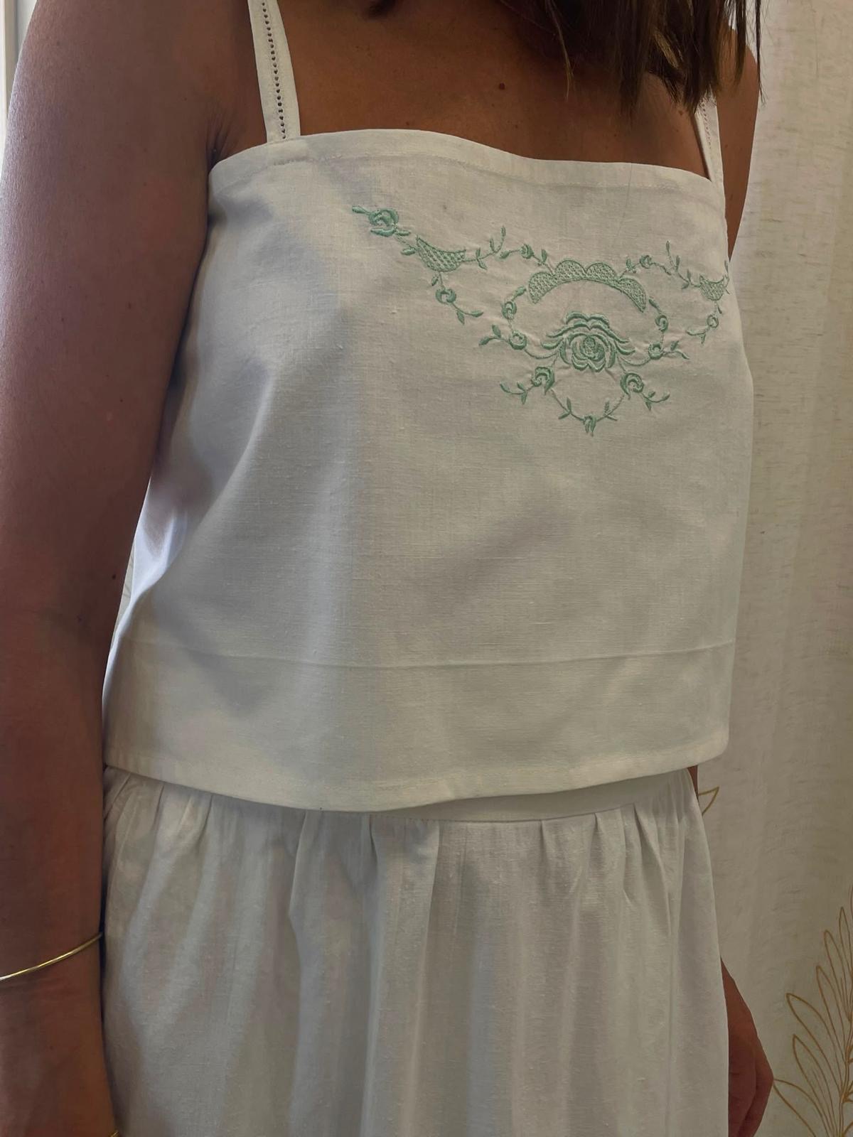 Close-up of mint green floral embroidery on the white linen top